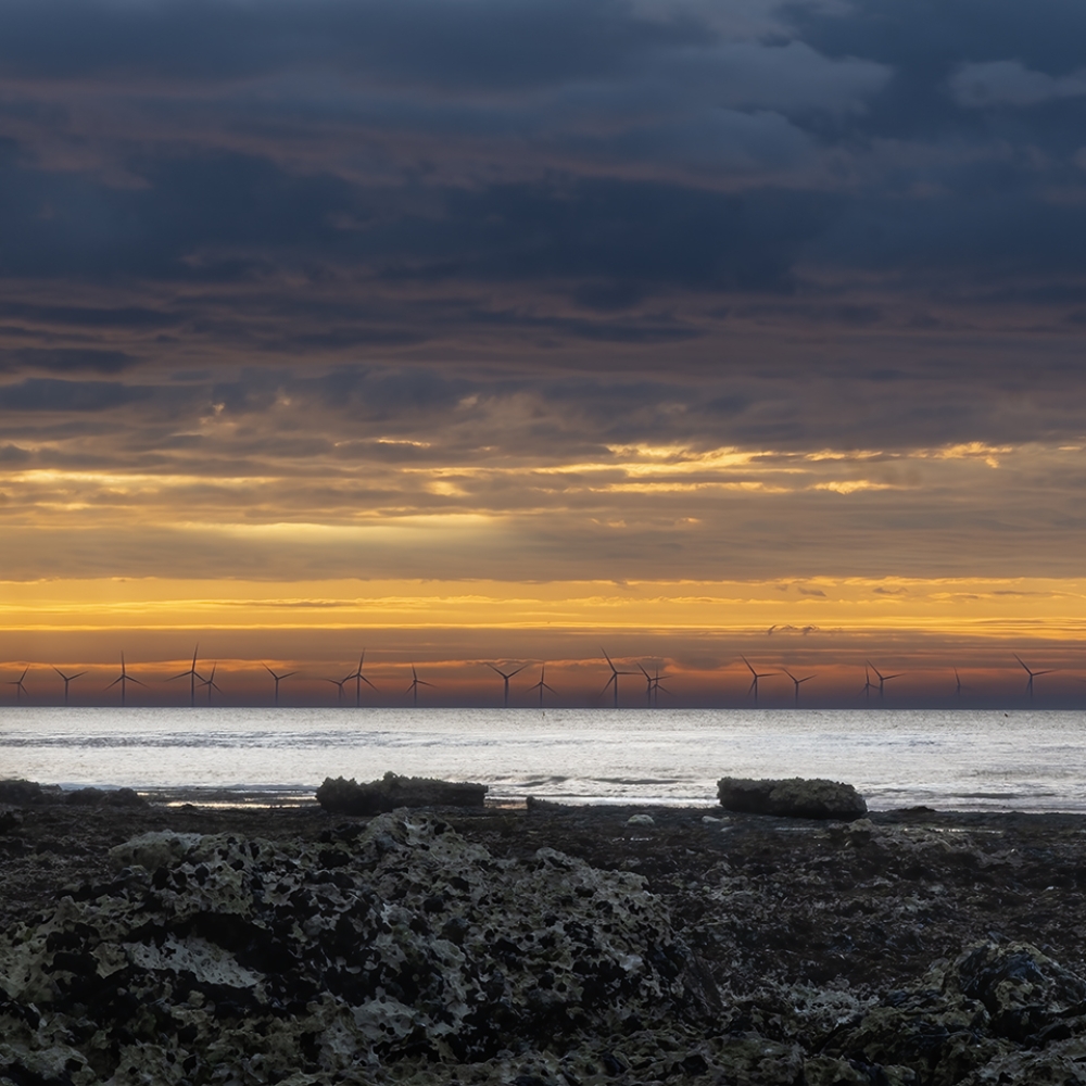 De zon gaat onder achter de windmolens voor de kust van Saint-Pierre in Normandië.